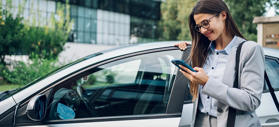 Mujer fuera de un coche, escribiendo en el móvil mientras abre la puerta del vehículo